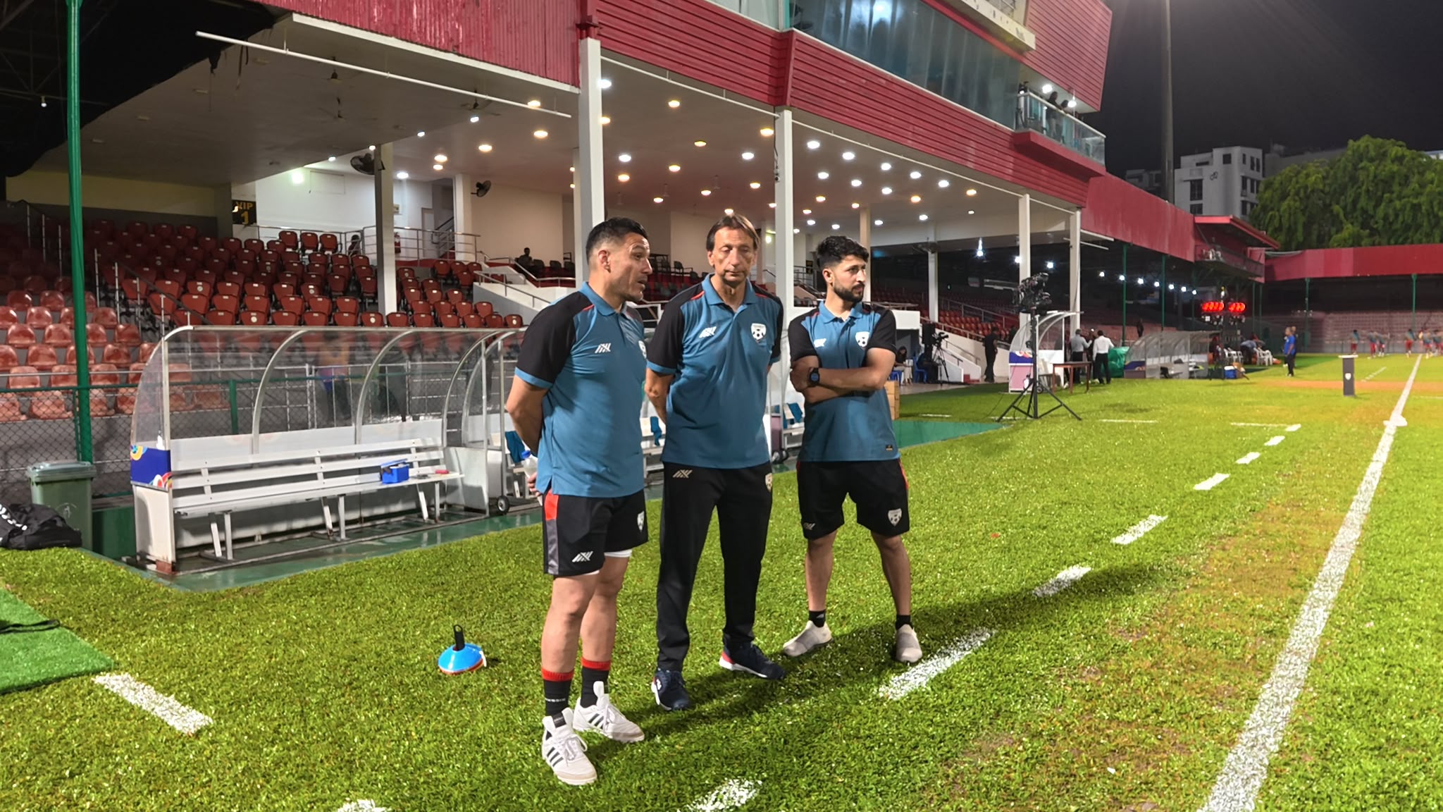 Amir Tamim Sultani pitchside with national-team medical staff at a floodlit stadium